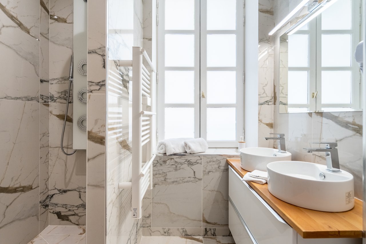 Chambre Deluxe : salle de bains en marbre avec double vasque, grand miroir et douche à l'italienne vitrée