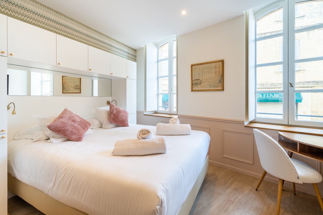 Chambre Deluxe : lit aux coussins rose poudré et fenêtres cintrées